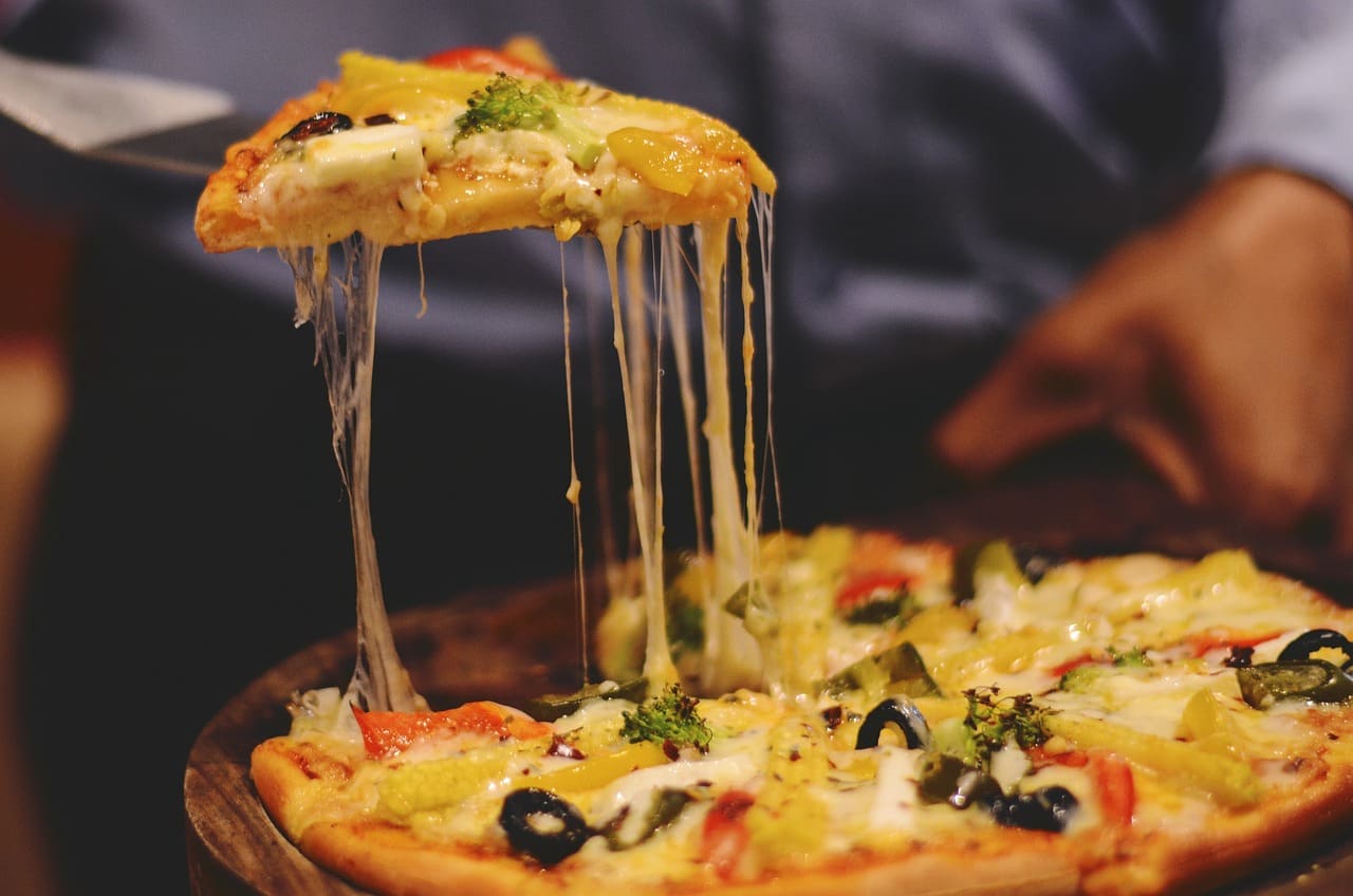 A slice being lifted from a fresh Millcreek pizza, cheese stretching